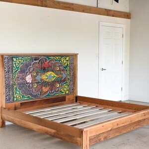 Puede incluir: Un marco de cama de madera con una cabecera de dise&ntilde;o colorido. La cabecera presenta un dise&ntilde;o geom&eacute;trico con tonos de verde, azul, amarillo y rojo. El marco de la cama est&aacute; hecho de madera reciclada y tiene un acabado natural.