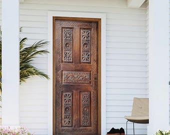 May include: A wooden front door with intricate carvings and a dark brown stain. The door is set in a white frame and has a white door handle. The door is surrounded by white siding and a white porch with steps. The number 3110 is written on the porch.