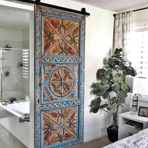 May include: A decorative wooden sliding door with a distressed finish. The door features intricate carvings and is painted in shades of blue, orange, and red. The door is mounted on a black metal track, adding a rustic touch to the room.
