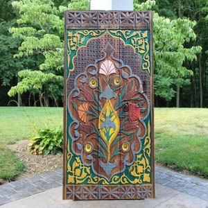 Puede incluir: Una puerta de madera tallada con intrincados dise&ntilde;os florales en tonos de verde, amarillo, rojo y azul. La puerta est&aacute; enmarcada con un borde de madera marr&oacute;n y tiene un patr&oacute;n geom&eacute;trico.