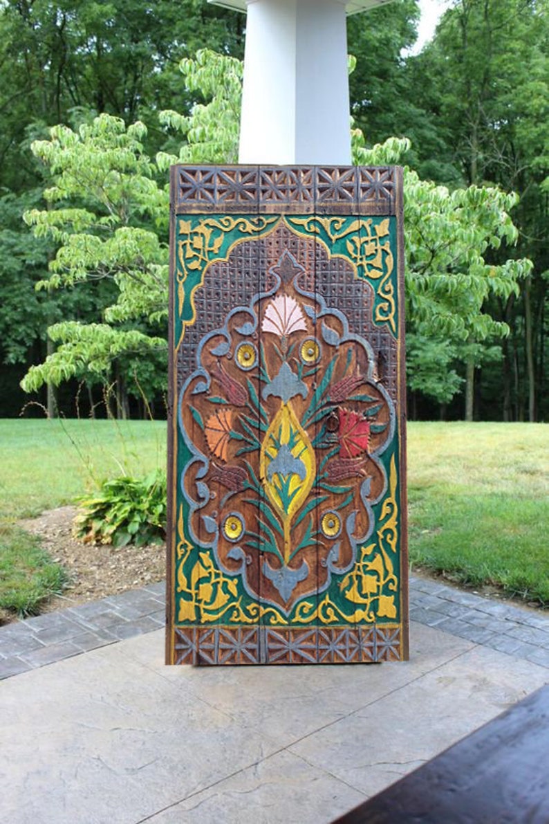 Puede incluir: Una puerta de madera tallada con intrincados dise&ntilde;os florales en tonos de verde, amarillo, rojo y azul. La puerta est&aacute; enmarcada con un borde de madera marr&oacute;n y tiene un patr&oacute;n geom&eacute;trico.