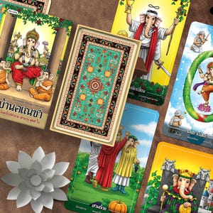 May include: A deck of cards with colourful illustrations of Ganesha, with Thai text. The cards are arranged with a decorative box and a white lotus flower. The cards have a teal and black patterned design.