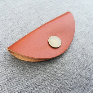 May include: A brown leather key holder with a metal button closure. The holder is shaped like a half-circle.