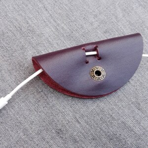 May include: A burgundy leather cord keeper with a brass button and a white cord threaded through it.