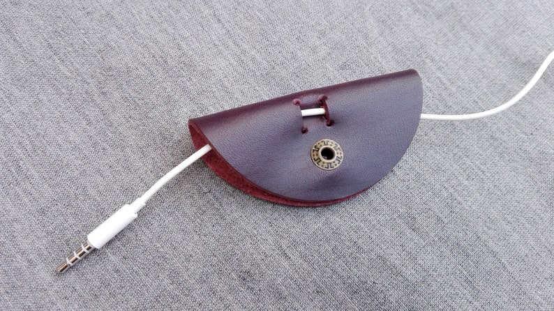 May include: A burgundy leather cord keeper with a brass button and a white cord threaded through it.
