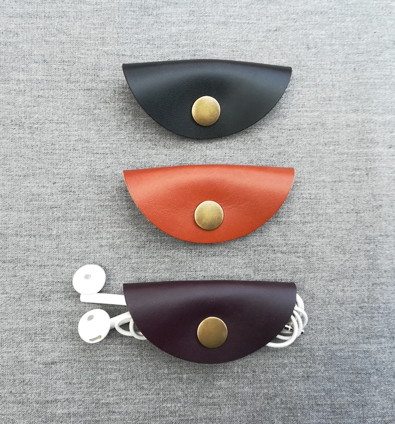 May include: Three leather cord organizers in black, orange, and purple. Each organizer has a brass button closure.