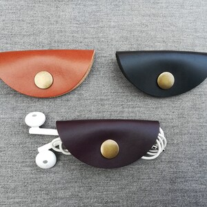 May include: Three leather cord organizers in brown, black, and burgundy. Each organizer has a brass button closure.