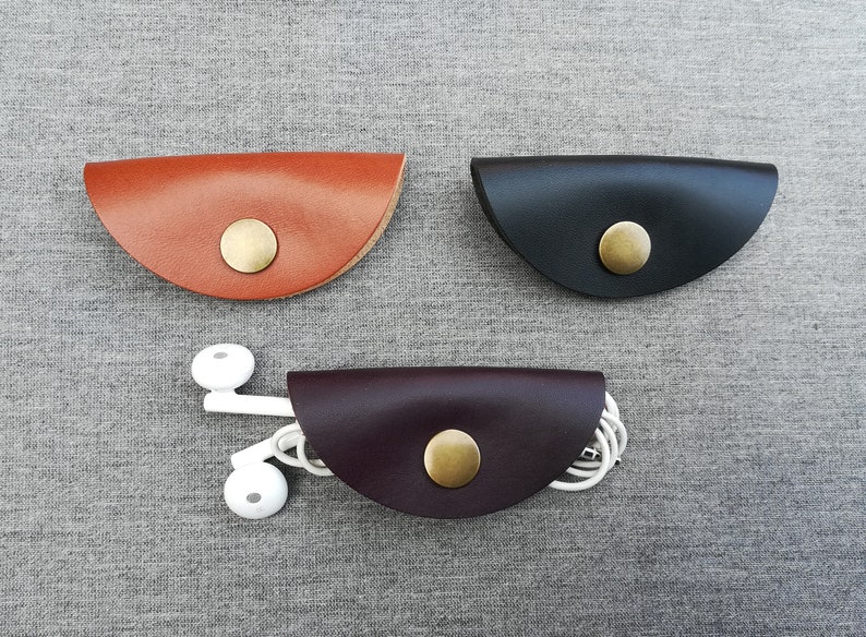 May include: Three leather cord organizers in brown, black, and burgundy. Each organizer has a brass button closure.