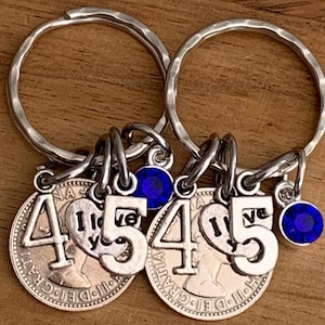 Könnte beinhalten: Zwei silberfarbene Schlüsselanhänger mit runden Metallmünzen mit der Zahl 45, einem herzförmigen Anhänger mit dem Text I love you und einem kleinen runden blauen Kristallanhänger an einem gehämmerten Metallring.