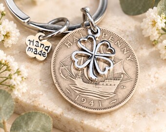 Puede incluir: Un llavero de metal plateado que incluye una moneda de medio penique de 1941, un dije de trébol de cuatro hojas y una pequeña etiqueta con forma de flor con el texto "hand made" grabado. La moneda muestra un velero y el año 1941.