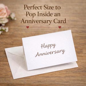Puede incluir: Una peque&ntilde;a tarjeta blanca doblada con el texto Happy Anniversary en fuente cursiva marr&oacute;n, descansando sobre un sobre blanco a juego. El texto sobre la tarjeta dice Perfect Size to Pop Inside an Anniversary Card con dos peque&ntilde;os corazones rojos.