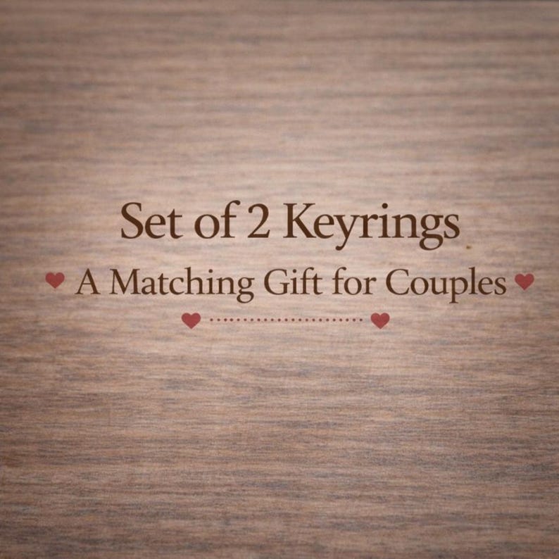 Puede incluir: Un fondo con textura de madera marr&oacute;n que presenta texto en marr&oacute;n oscuro que dice Set of 2 Keyrings, A Matching Gift for Couples, acentuado por cuatro peque&ntilde;os iconos de corazones rojos y una l&iacute;nea punteada entre los dos corazones inferiores.