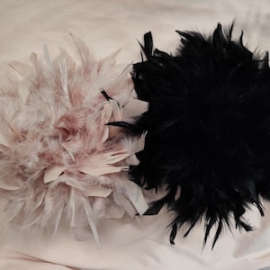 May include: Two feather embellishments, one in soft pink and the other in black. The pink one has a mix of pink and white feathers, while the black one is a dense cluster of dark feathers. Both are round in shape.