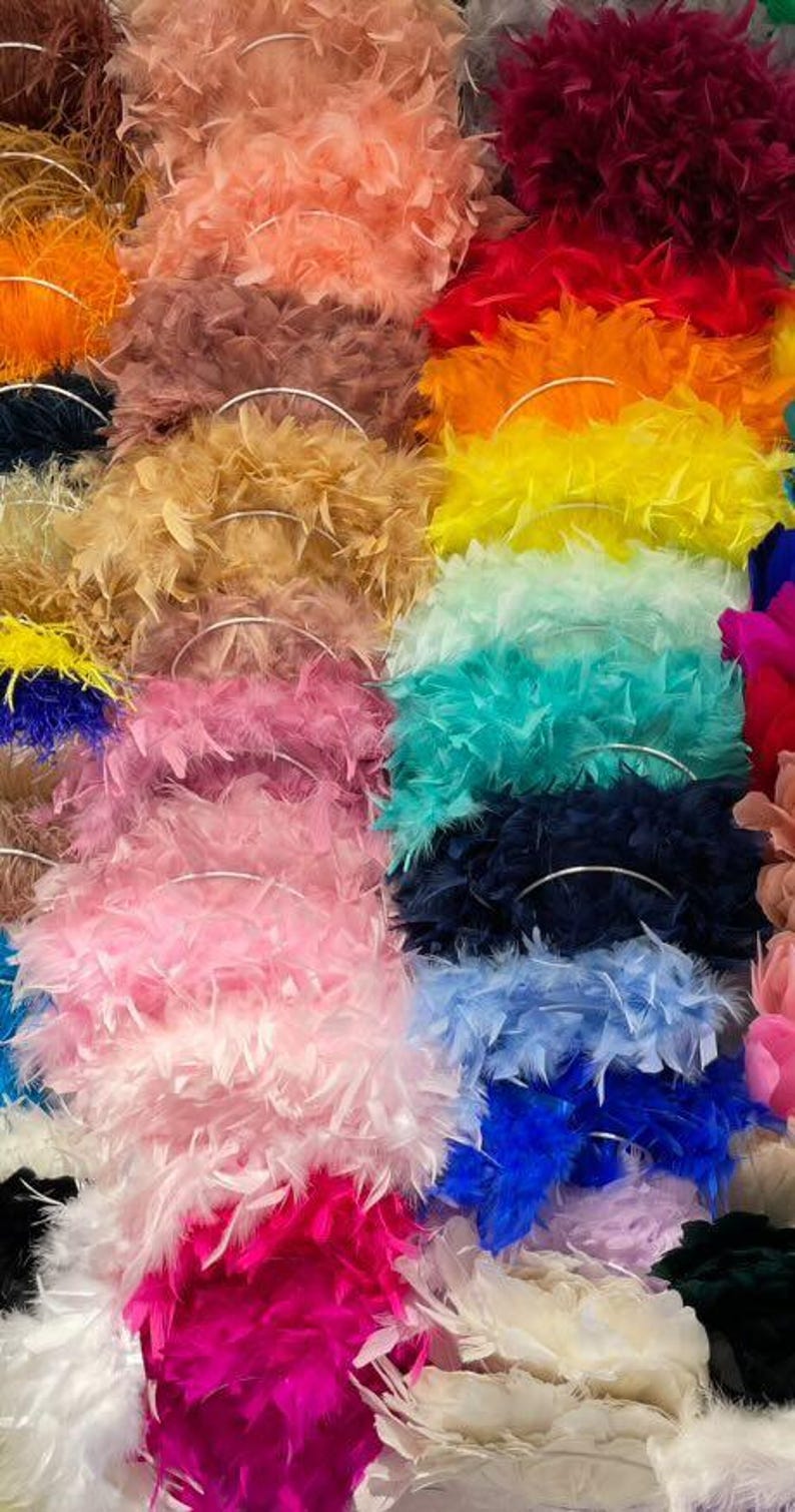May include: A vibrant display of feather boas in various colors, including pink, blue, yellow, and orange. Each boa is arranged in a circular shape, showcasing the fluffy texture and rich hues. The image highlights the diversity of colors and the soft, voluminous nature of the feather boas.
