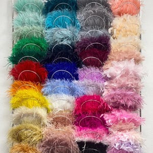 May include: A display of colorful feather boas in various shades, including teal, emerald green, red, and pink. The text "CHOOSE YOUR PERFECT SHADE" is at the top. Each boa is attached to a silver wire ring.