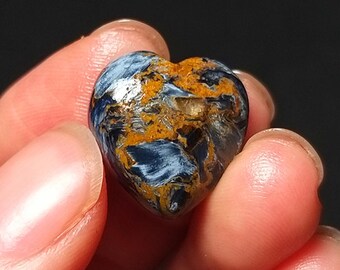 Könnte beinhalten: Ein herzförmiger Edelstein mit einer Mischung aus blauen und goldenen Farben. Der Stein wird zwischen Fingern gehalten, was seine polierte Oberfläche und einzigartigen Farbmuster hervorhebt. Der Edelstein ist ein natürliches Mineral, perfekt für Schmuck oder Sammlungen.