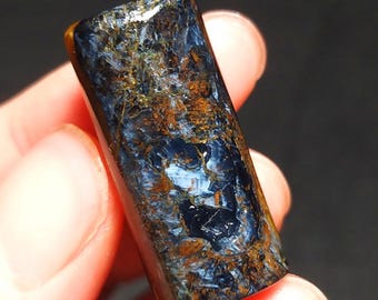 May include: A blue and gold tiger's eye gemstone, polished and shaped into a cylinder. The stone has a unique pattern of blue, gold, and brown.