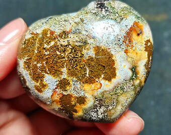 May include: A heart-shaped polished stone with a variety of colors, including brown, white, green, and orange. The stone has a unique, mottled pattern.