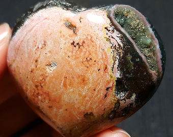 May include: A heart-shaped polished stone with pink, green, and brown swirling patterns. The stone has a smooth, polished surface.