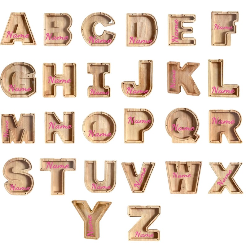 Peut inclure: Une collection de vingt-six tirelires en bois en forme de lettres, chacune dot&eacute;e d'une fa&ccedil;ade transparente et du mot Name imprim&eacute; en &eacute;criture rose. Les lettres de A &agrave; Z sont dispos&eacute;es en grille, r&eacute;v&eacute;lant le grain du bois clair naturel.