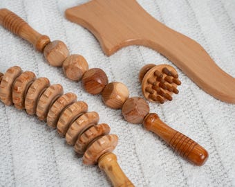 May include: A collection of wooden massage tools, including a roller, a ball massager, a small round massager with pegs, and a curved wooden tool. The tools are made of light brown wood and are arranged on a white surface.