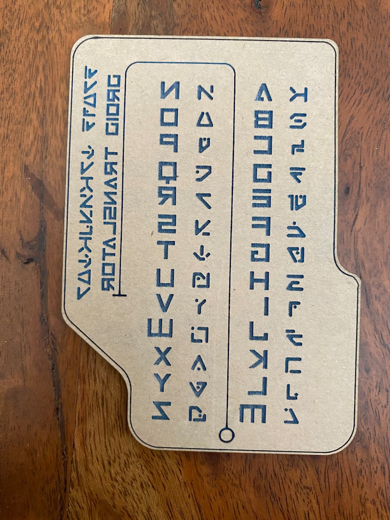 May include: A brown card with a blue alphabet printed on it. The alphabet is in a stylized font and includes the letters A through Z. The card also includes the text "ROYAL SMART GIORG".