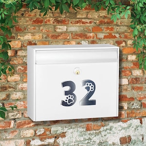 May include: White metal mailbox with a black number 32 with paw prints on the mailbox. The mailbox is mounted on a brick wall.