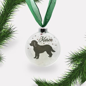 May include: A white glass Christmas ornament with a black silhouette of a dog and the name "Mason" written in cursive. The ornament is decorated with small white snowflakes.