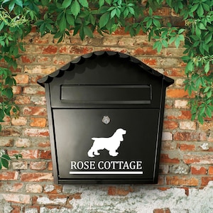 Puede incluir: Buzón negro con una silueta blanca de un perro y el texto "ROSE COTTAGE" en la parte delantera.