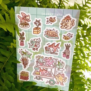 Puede incluir: Una hoja de pegatinas con lindas ilustraciones de dibujos animados de tiburones, plantas y otras criaturas marinas. Las pegatinas est&aacute;n sobre un fondo azul claro con un patr&oacute;n de cuadr&iacute;cula. El texto "SHARKTEATH" est&aacute; impreso en la esquina superior derecha de la hoja.