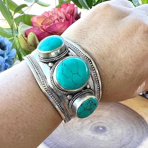 Puede incluir: Un brazalete de plata con tres piedras turquesa. Las piedras son redondas y tienen un patrón de mármol. El brazalete es ancho y tiene un diseño decorativo.