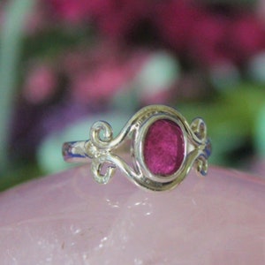 May include: A silver ring with a pink gemstone set in a delicate, ornate design.
