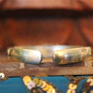 K&ouml;nnte beinhalten: Ein silbernes Armreif-Armband mit glatter, polierter Oberfl&auml;che. Das Armband ist an einer Seite offen und hat eine leicht gebogene Form.