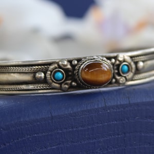 May include: Silver bangle bracelet with a tiger's eye gemstone and two turquoise stones.
