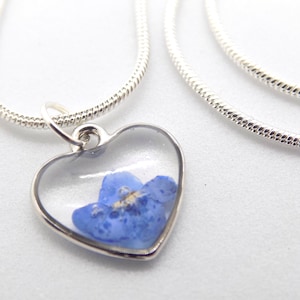May include: A silver chain necklace with a heart-shaped pendant. The pendant is clear and contains a pressed blue flower.