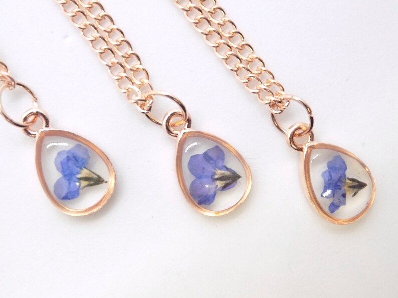 Puede incluir: Tres collares de oro con colgantes en forma de l&aacute;grima que contienen flores azules prensadas.