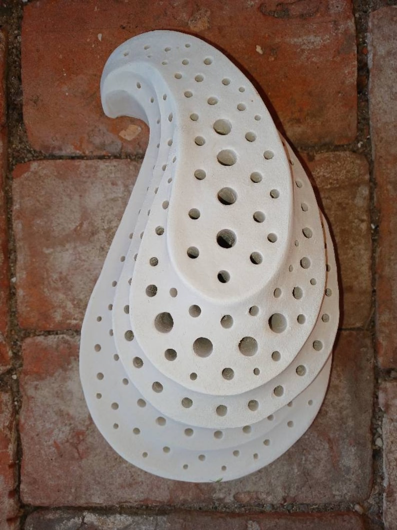 May include: White ceramic teardrop-shaped object with multiple layers of circular holes. The object is made of white ceramic and has a smooth, matte finish.