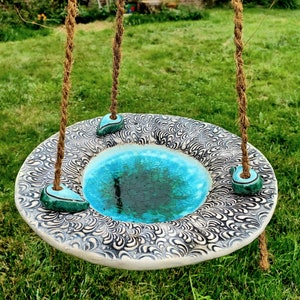 Puede incluir: Un baño de pájaros de cerámica con un esmalte azul y verde. El baño está suspendido de una cuerda y tiene un patrón decorativo.