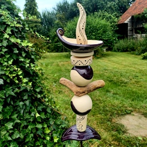 Può includere: Una scultura da giardino in ceramica con un design fantasioso. La scultura è realizzata in ceramica bianca e viola e presenta una cima alta e appuntita con una forma curva a forma di foglia. La scultura è decorata con motivi in ​​bianco e nero.