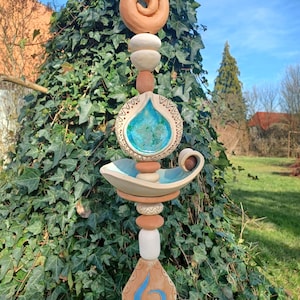 Może przedstawiać: Ceramiczna palik ogrodowa z wzorem błękitnej i białej łzy, brązową spiralą i białymi i brązowymi koralikami. Palik jest umieszczony na tle zielonego bluszczu.