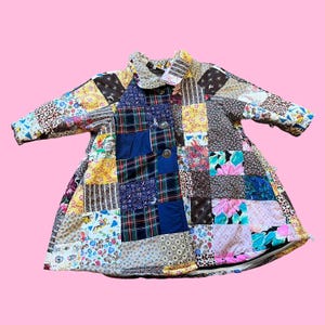 May include: A patchwork coat featuring a variety of fabric patterns and colors, including floral, plaid, and solid patches. The coat has a rounded collar, button closure, and long sleeves. The coat is a unique, handmade garment.
