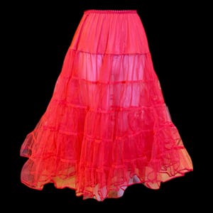 May include: A bright red petticoat skirt with multiple layers of tulle and a satin lining. The skirt has a wide waistband and a full, flared silhouette. The layers create volume and movement, perfect for vintage-inspired outfits.