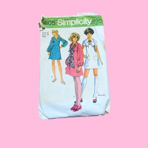 May include: A Simplicity 8805 sewing pattern envelope featuring illustrations of three different dress styles. The white paper envelope displays the text Simplicity 8805, Size 12, Bust 34, and 85c. The dresses shown include a blue polka dot dress, a pink dress with a patterned scarf, and a white dress.