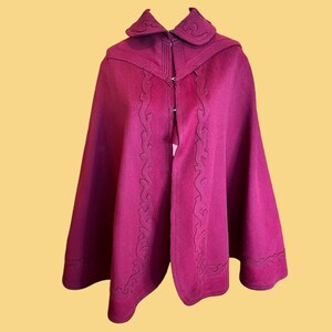 May include: A deep burgundy wool cape with a high collar and intricate embroidered detailing around the edges.