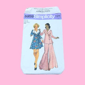 May include: A Simplicity 5959 sewing pattern envelope featuring illustrations of two outfits: a blue floral print dress with a white collar and a pink patterned long-sleeved jacket with matching wide-leg trousers. The text includes size 12, bust 34 inches, and waist 26.5 inches.