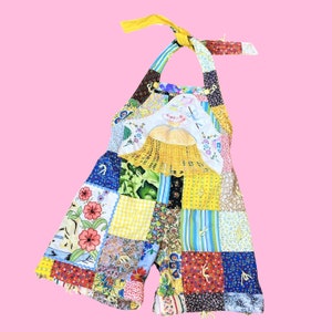 May include: A patchwork overall romper with a yellow crocheted detail and floral embroidery. The romper is made of various colorful fabrics and has a halter neck style.