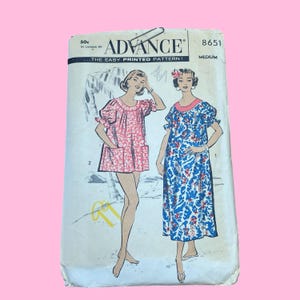 May include: Vintage Advance sewing pattern packet featuring illustrations of two dresses. The packet is cream-colored with the text "ADVANCE" and "THE EASY PRINTED PATTERN!" printed in black. The illustrations depict a short pink dress and a long blue dress with floral patterns.