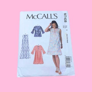 May include: A McCall's M7408 sewing pattern envelope for a sleeveless or three-quarter sleeve dress with a split neckline. The cover displays four variations of the dress in different colors and patterns, including blue, orange, and multi-colored prints.