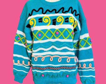 May include: A turquoise sweater with a crew neck and long sleeves. The sweater features a colorful design with white stripes, black squiggles, yellow swirls, green diamonds, pink dots, and peach-colored loops. The sweater is a unique and eye-catching piece of clothing.