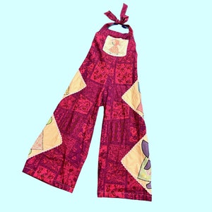 May include: Pink patchwork jumpsuit with a halter top and a colorful print. The jumpsuit has a square pattern with different colors and designs.